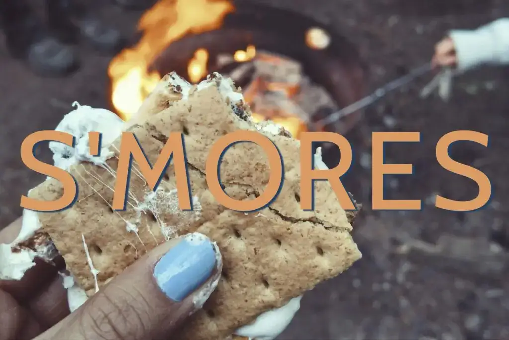 Text that reads "S'mores" overlayed on an image of a woman's hand holding a s'more with marshmallow oozing out the sides.