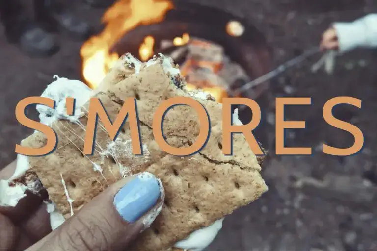 Text that reads "S'mores" overlayed on an image of a woman's hand holding a s'more with marshmallow oozing out the sides.